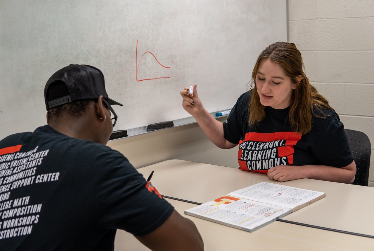 student showing math problem on board for another student