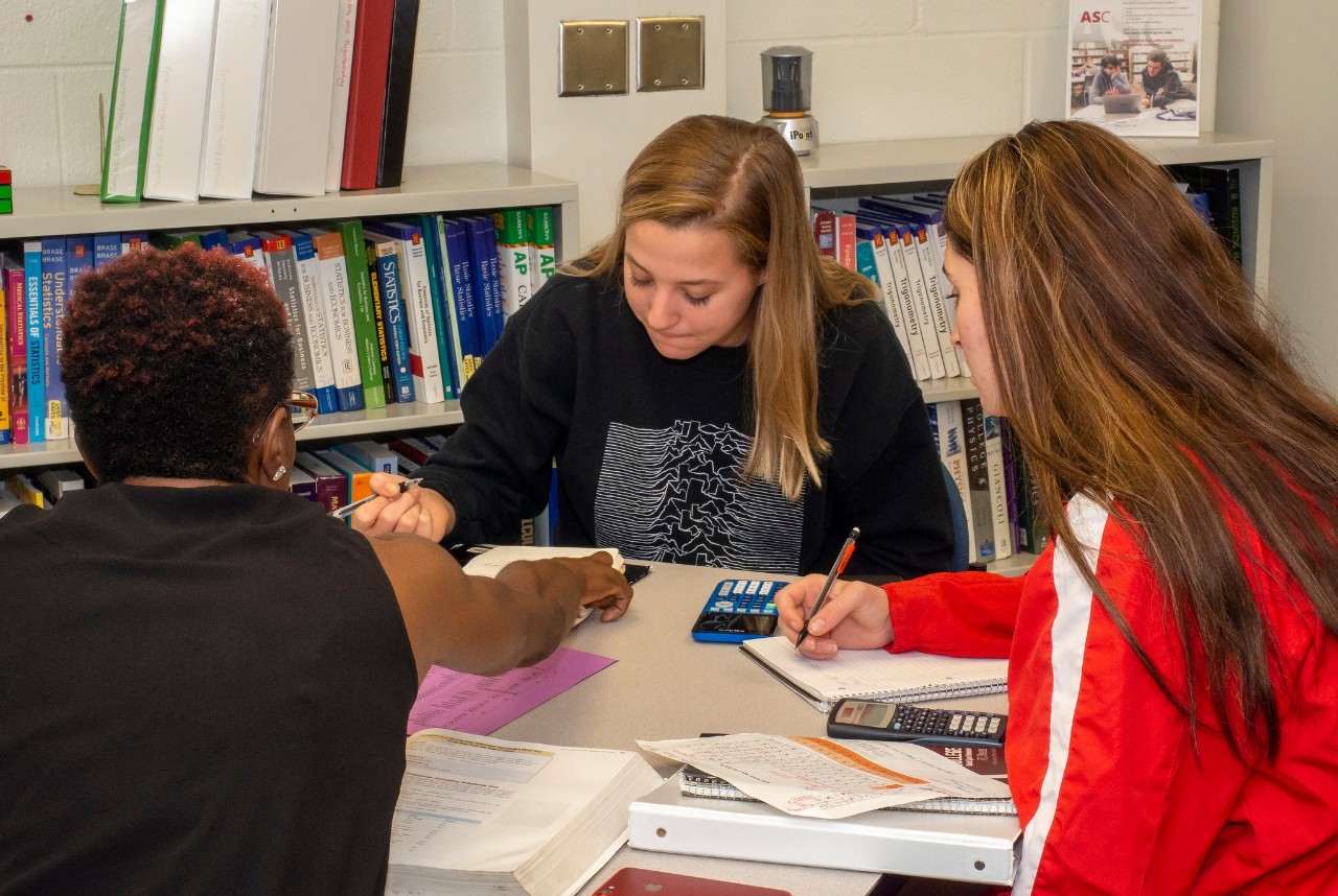 3 people sitting at a table doing homework together